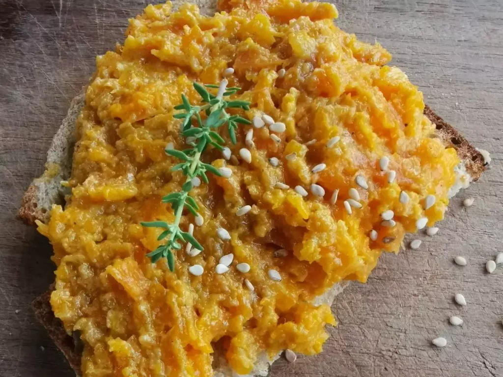 Een boterham met oranje wortelspread en sesamzaadjes als topping.